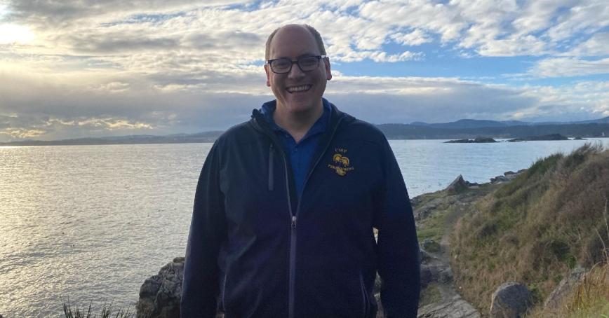 Andrew Delong standing on the beach with the ocean behind him.