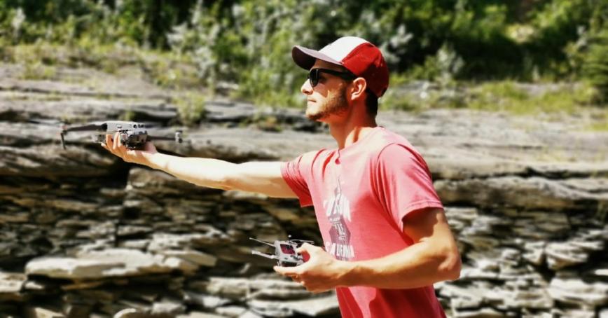 Jared Matlock, arm outstretched and holding a drone on a rocky shore.