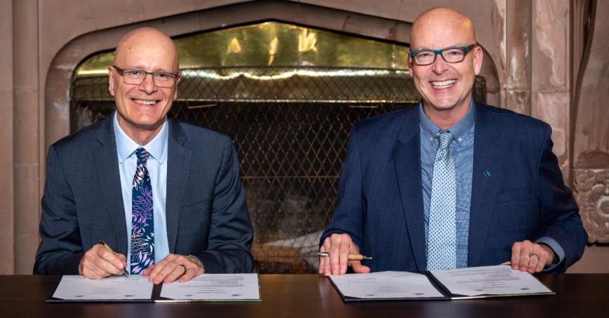 Philip Steenkamp and Tim Rahilly seated at a desk, signing a memorandum of understanding.