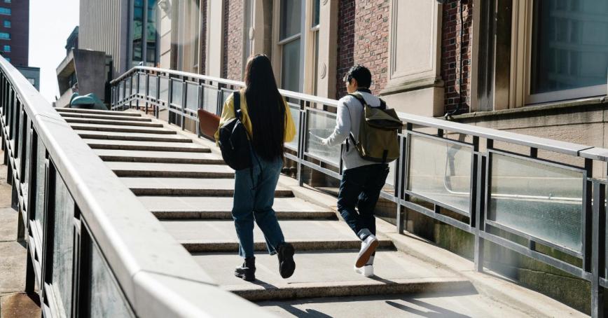 Two university students walk up concrete steps outside in an urban area