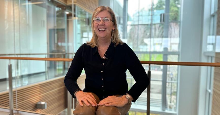 A woman laughs while sitting indoors, in front of a hallway window