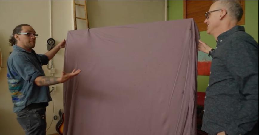 Tl'azt'en artist Damian John unveils his painting as RRU professor Geo Takach’s looks on.