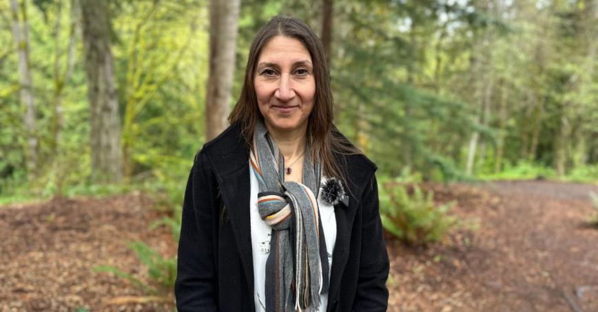A woman smiles for a head shot, a forested scene behind her.