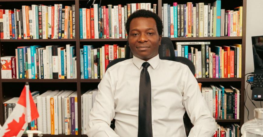 Dapo Bankole sitting in front of a large bookshelf filled with books.