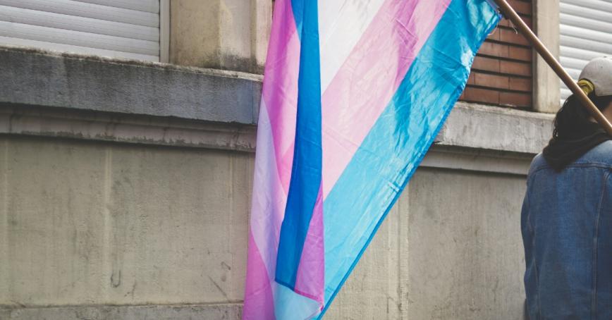 Person walking with a large transgender pride flag hanging over their shoulder