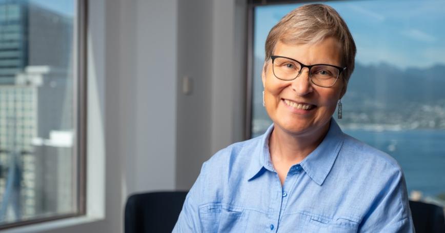 Lori Wanamaker wears a blue collared shirt, has short hair and glasses and is smiling.