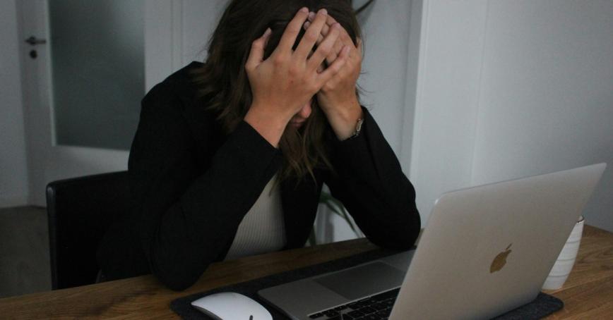 Woman holding her head in her hands with an open laptop in front of her.