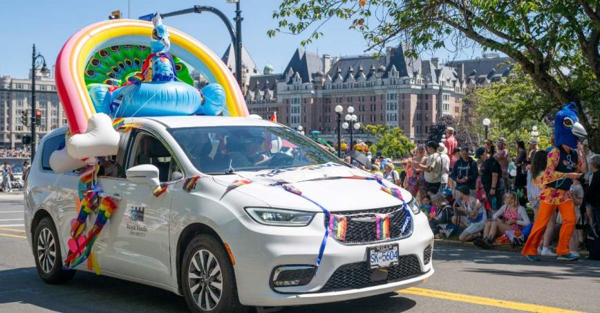 Royal Roads white van decorated for Pride with an inflatable rainbow and peacock attached to its roof.