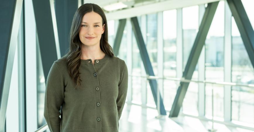 Paige Mason is standing next to a wall of windows wearing a green sweater.