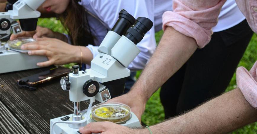 Two students using microscopes to look at specimen in an outdoor setting
