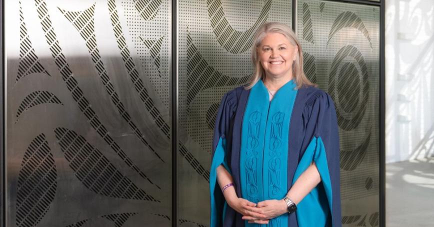 Jody Thomas stands outside of the Dogwood Auditorium wearing convocation robes.