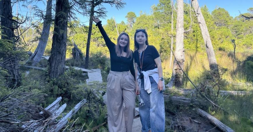 Two young students pose for a photo in a forested area.