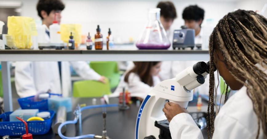 A student looking into a microscope in a laboratory environment with other students working in the background