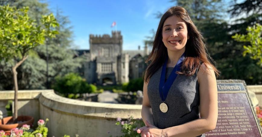 A woman poses with a metal on blue ribbon in front of a stone castle.