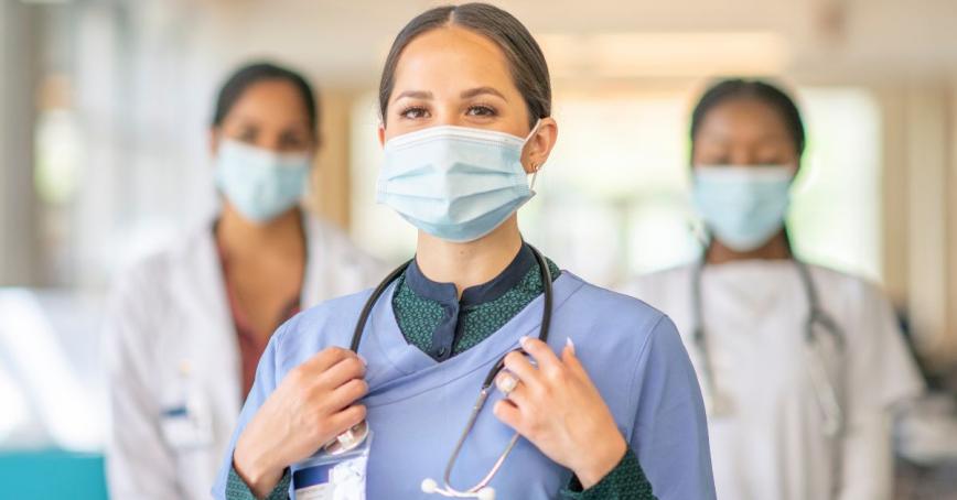 Three nurses stand in a hospital environment wearing scrubs and stethoscopes
