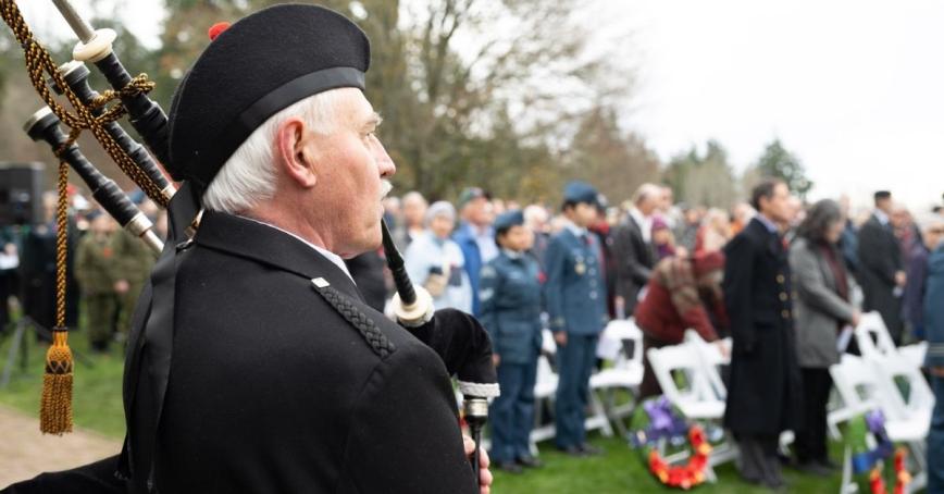 A bagpiper seen from behind while playing for a crowd gathered in remembrance