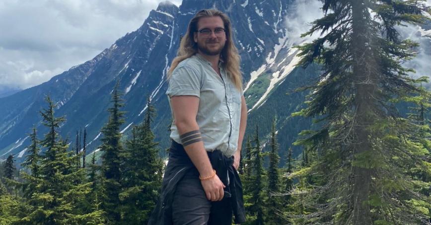 Brian Lawless standing outdoors with mountain peak and trees in the background.