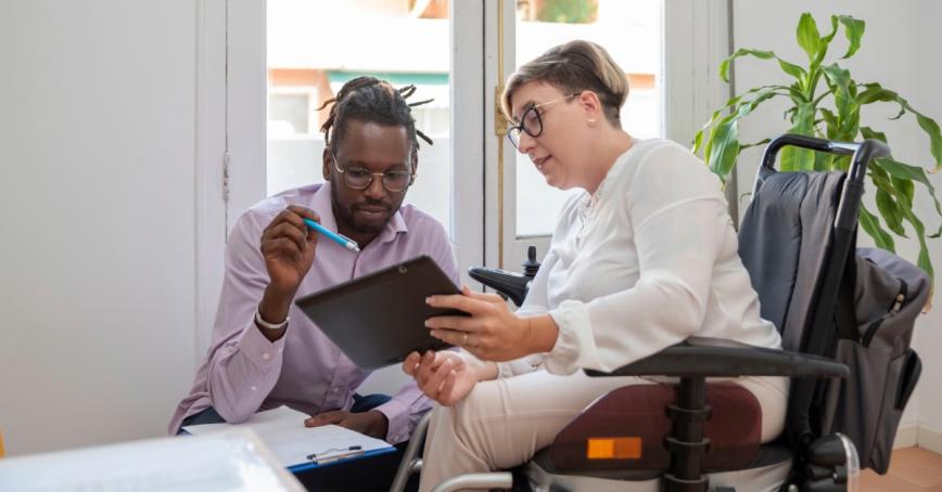 A woman in a wheelchair speaks with a medical professional while looking at an Ipad