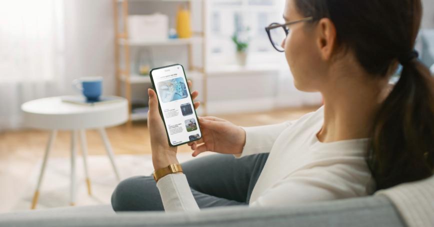 A woman sitting and looking at a news app on her phone