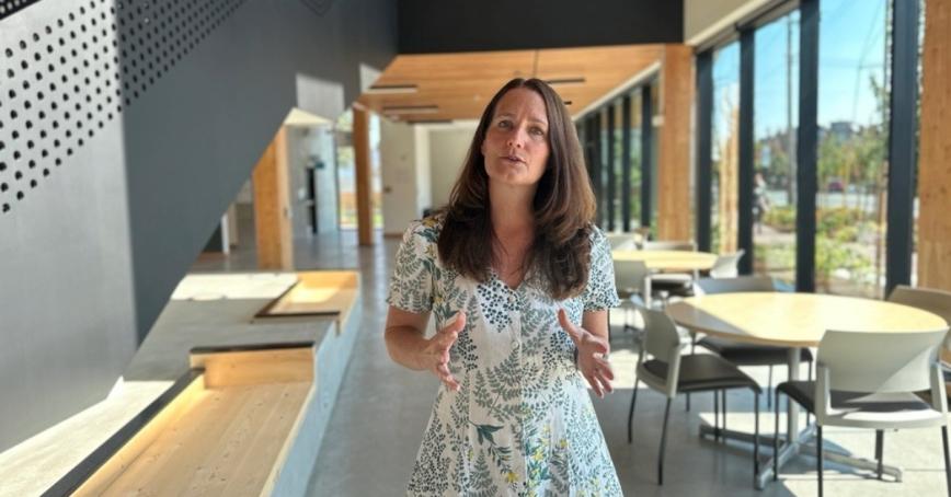 A woman in a floral dress looks to the camera as she's speaking.