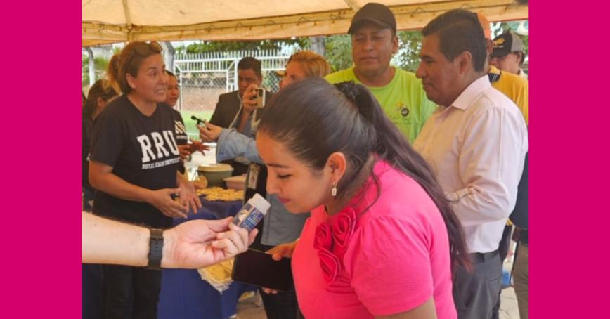 Woman wearing a bright pink t-shirt smells a spice jar being held out to her.