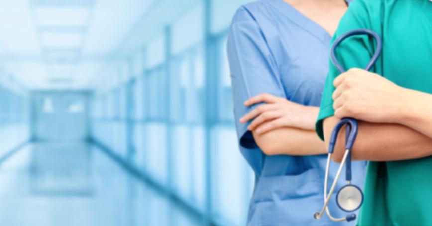 Two doctors shown in scrubs, one is holding a stethoscope, standing in a long glass hallway.