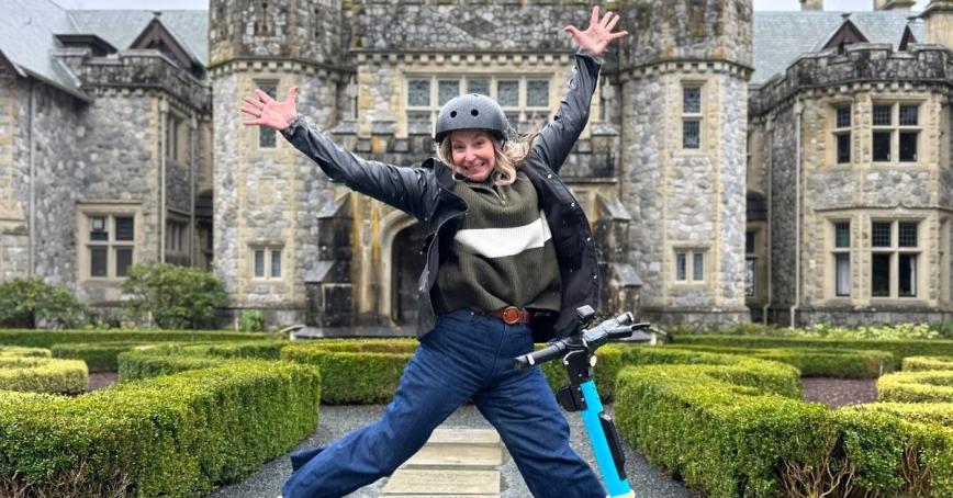 Karly Nygaard-Peterson jumping in front of Hatley Castle, with a helmet and an e-scooter