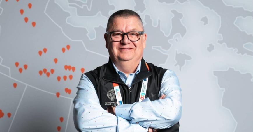 Dan George smiling with arms crossed in front of a map mural