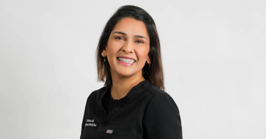 Dr. Huma Ali wearing scrubs and smiling in front of a white background. 