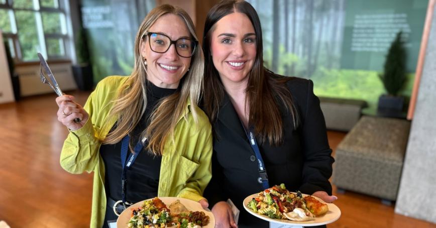 Two students smile at the camera while holding plates filled with perogies, cabbage rolls and salad.