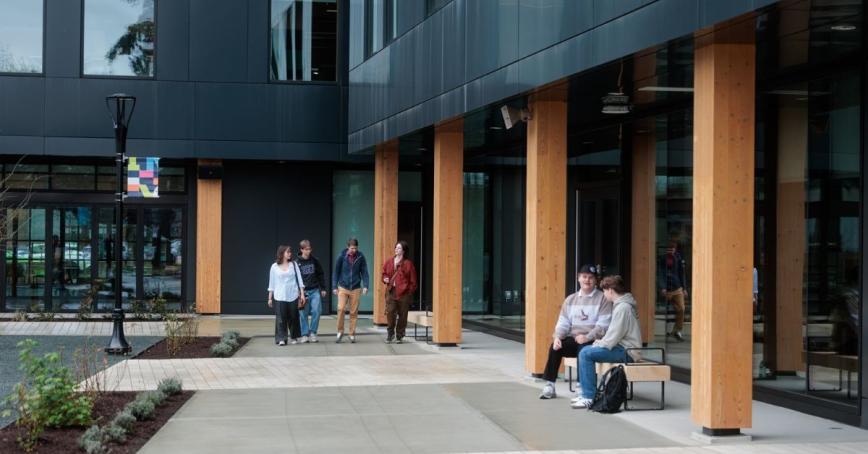 Groups of students can be seen sitting and walking on a university campus.