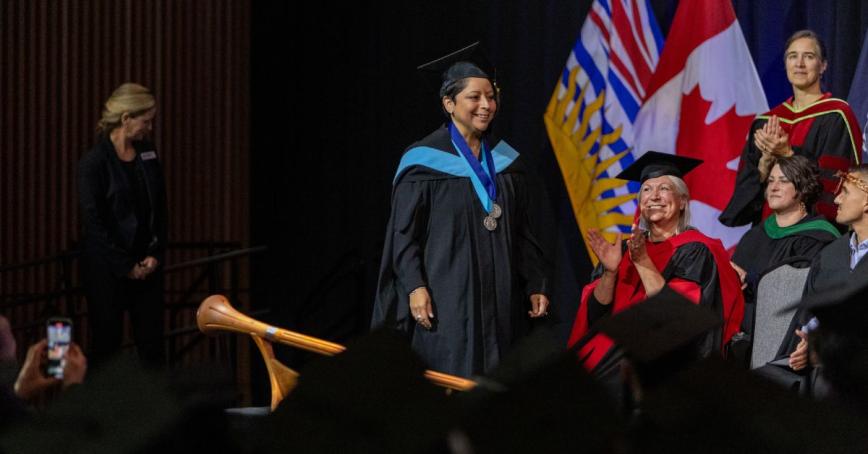 A graduate crosses the convocation stage, wearing two medals.