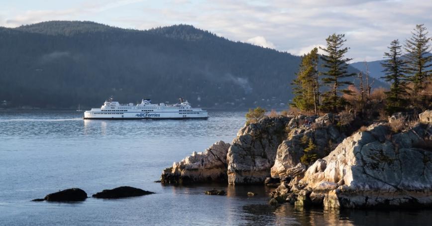 A BC Ferry passes by a rocky outcropping on calm waters