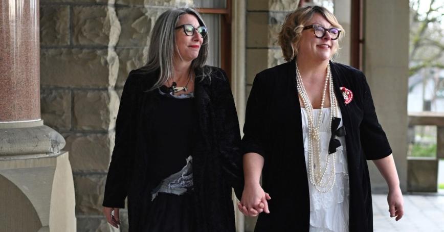 Two woman look over their shoulder while holding hands.