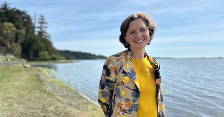 A smiling woman in a yellow top poses on a forested beach.