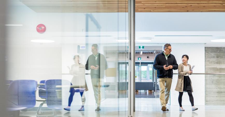 Two researchers walk through an empty hallway in discussion