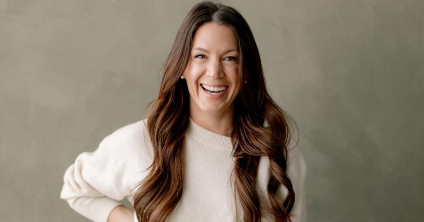 A woman poses for a headshot smiling and leaning in toward the camera.