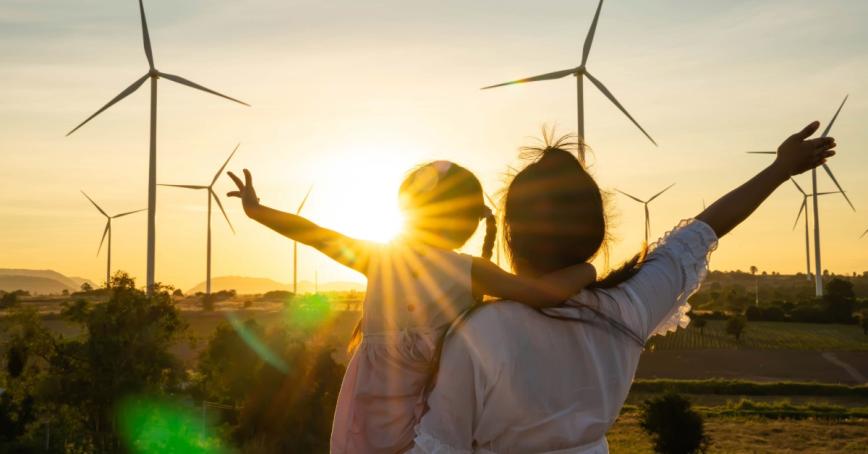 A mother and daughter watch the sunset at a wind farm