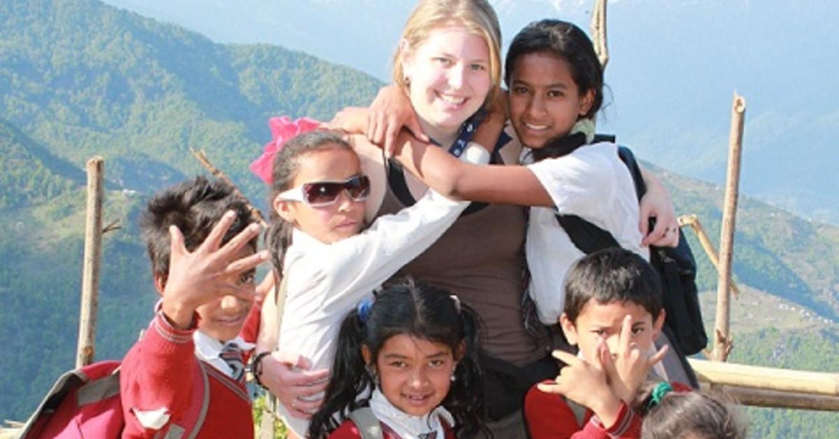 An RRU student standing with a group of young kids in front of a mountain backdrop