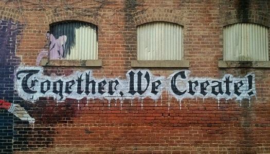 Words, "together, we create!" painted on side of brick building.