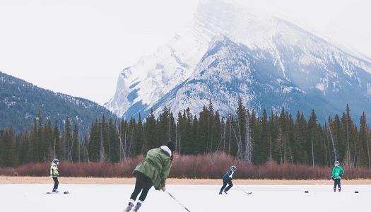 people playing hockey on a lake with trees and mountains around them.