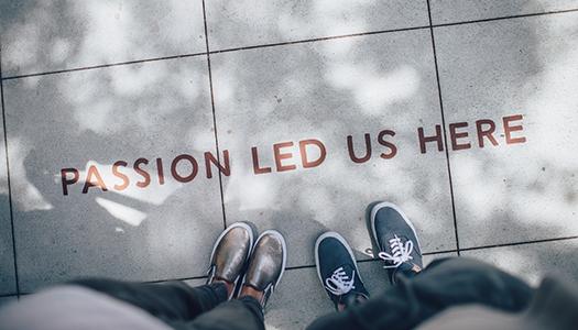 Two people looking down at "Passion led us here" writing on the sidewalk.