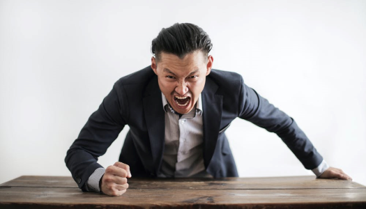 Person looking angry with fist hitting desk and looking like yelling.