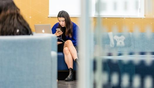 seated-student-looking-at-phone-with-laptop-beside-her