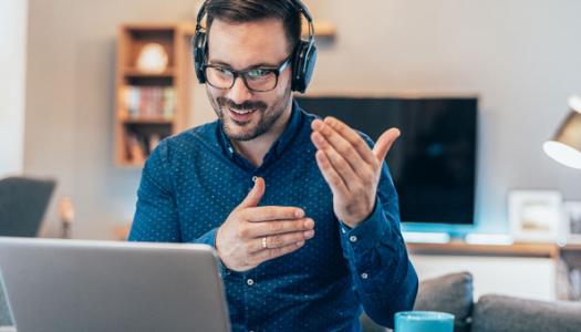 Person with headphones in living room presenting information to laptop screen