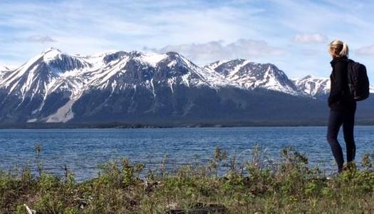 Person looking at water with mountains capped in snow in the distance.