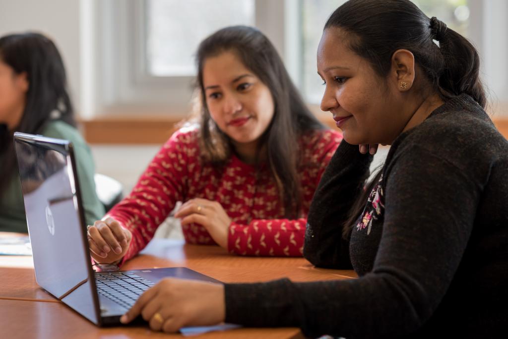 Two seated students look at a laptop screen in a Royal Roads classroom.