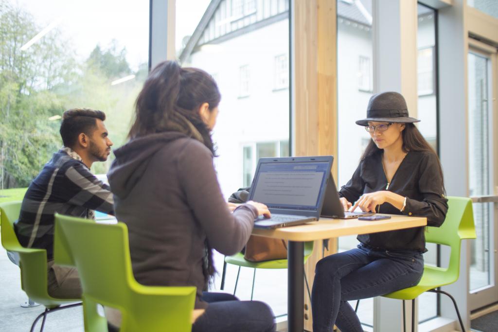 Three students work on laptops at table in Sherman Jen Building.