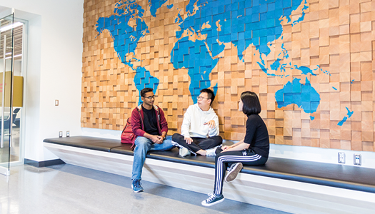 Three people sitting on a ledge by a blue map hung on the wall