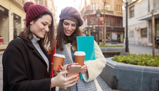 Two people smiling at a phone in front of an outdoor urban landscape